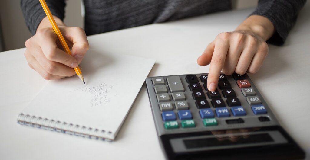 primer plano de manos usando una calculadora y escribiendo números en un block de notas