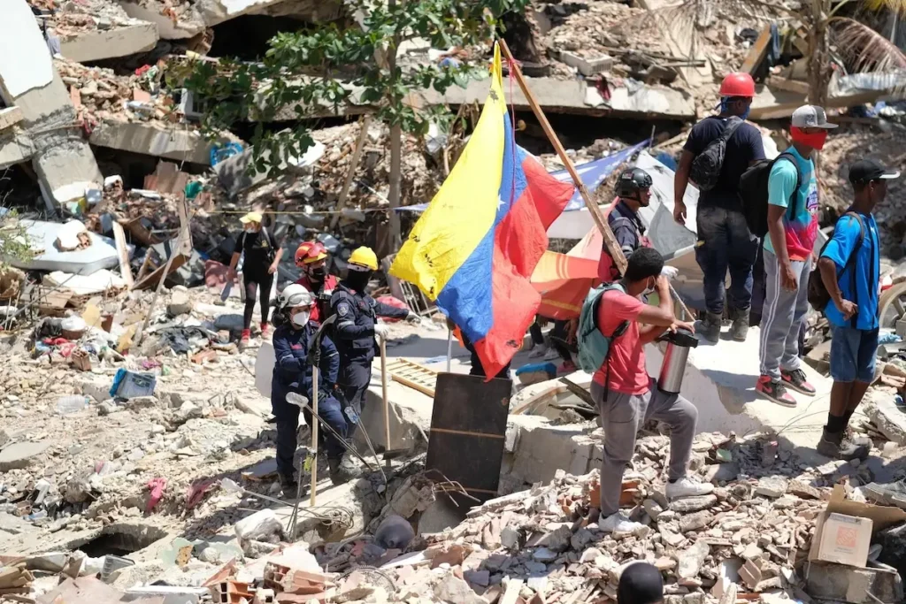 Equipos de rescate y voluntarios buscando sobrevivientes entre los escombros con una bandera de Venezuela.